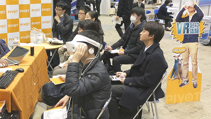 写真：採用イベントの出展ブースにて、学生が椅子に座りVRを視聴している。