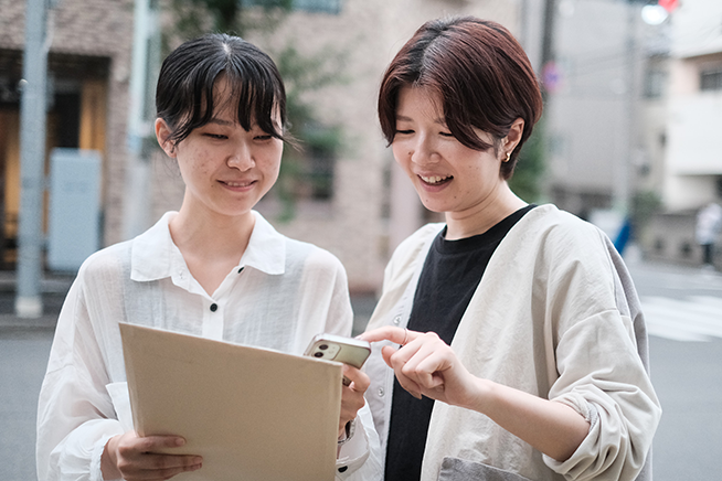 学びの特徴「探究心・好奇心を喚起する」をイメージした写真。街中で二人の人がデバイスを見ながら会話している様子。
