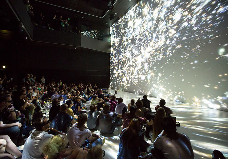 写真：巨大なスクリーンに映し出される映像作品を、地面に座って見ている参加者たち