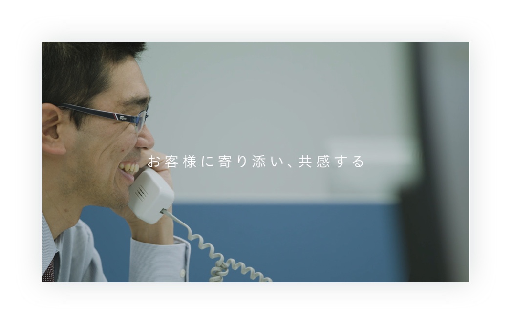 制作した動画のキャプチャ（8枚中7枚目）：電話応対する笑顔の富安の社員の様子。その画面の上に「お客様に寄り添い、共感する」の文字が書かれている。