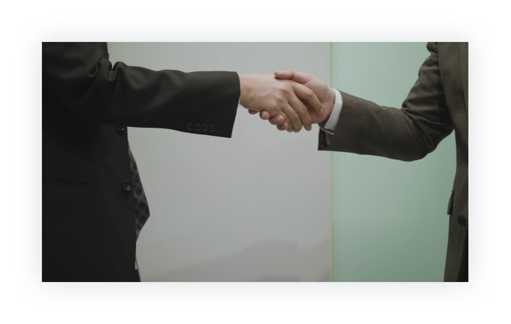 制作した動画のキャプチャ（8枚中8枚目）：握手をするスーツ姿の富安の社員と取引先の人物の手元。