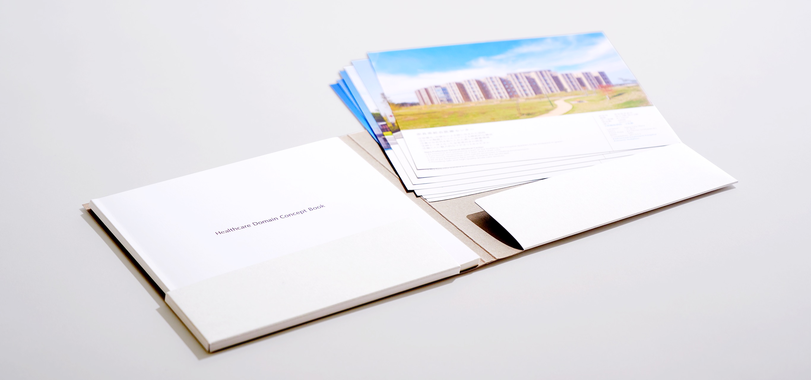 写真：制作したグレーのタトウ（二つ折りのポケットファイル）に収納されたパンフレットと事例カードのセット。