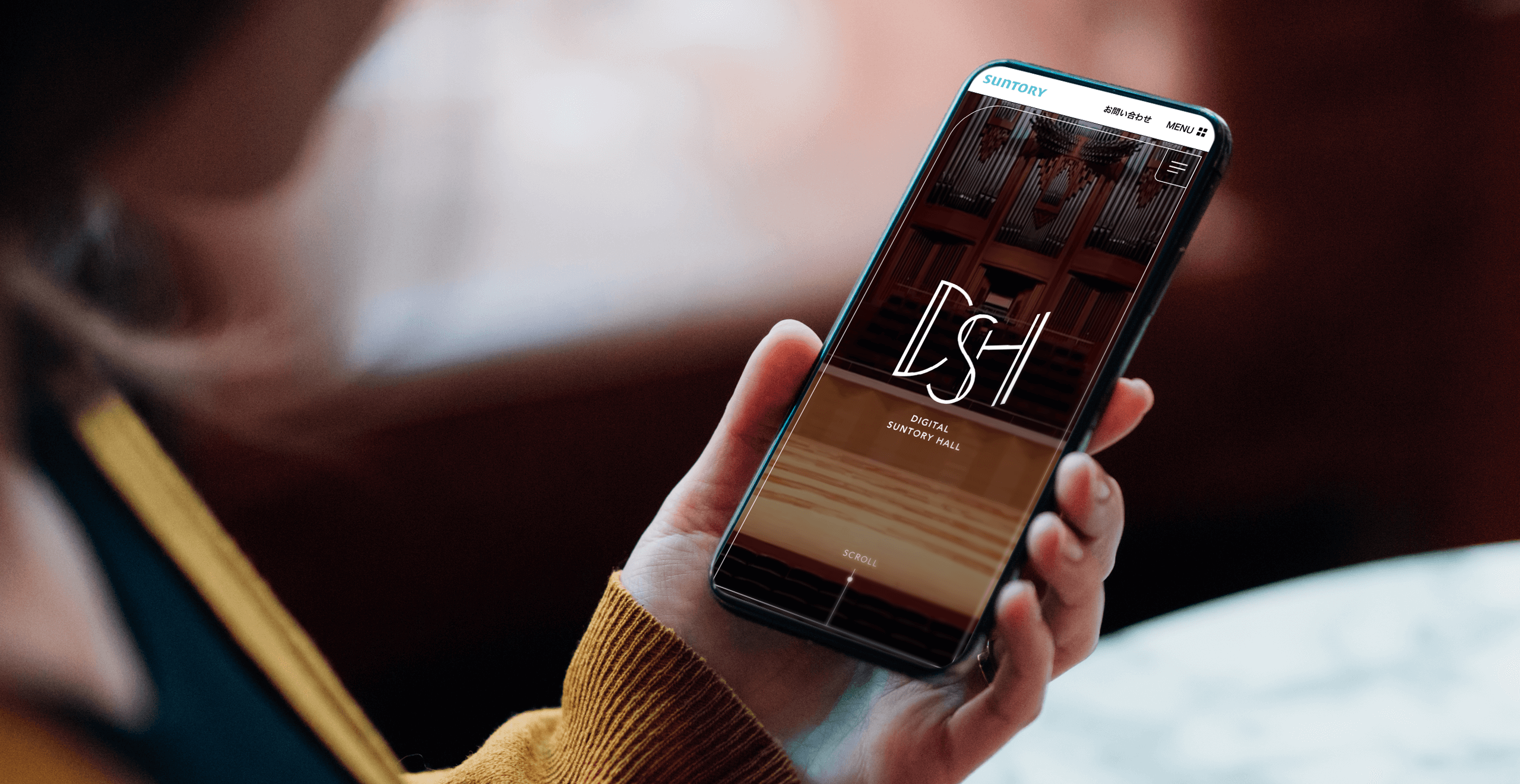 画像：女性がスマートフォンを片手に持ち、デジタルサントリーホール ウェブサイトのトップページを見ている。
