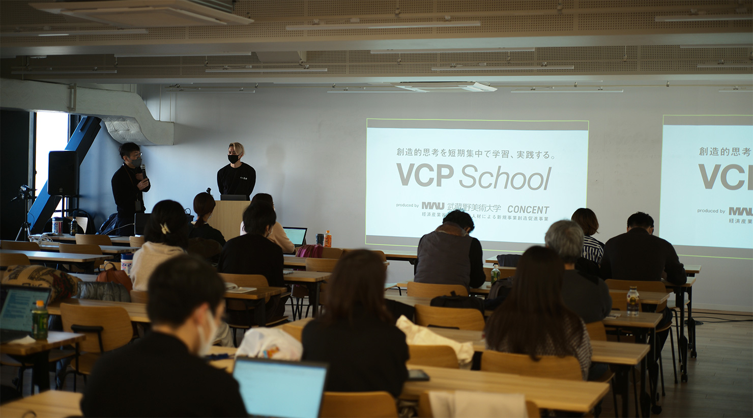 「価値創造人材育成プログラム（VCP）」実施中の画像。教室に講師や運営メンバー、複数の受講者がいる。教室前方の壁には「VCP School」の表題のスライド資料が映し出されている。