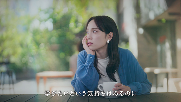 TVCMのキャプチャ:8枚中2枚目。カフェで女性がコーヒーカップを持ちながら、外を見やる。テロップ「学びたいという気持ちはあるのに」