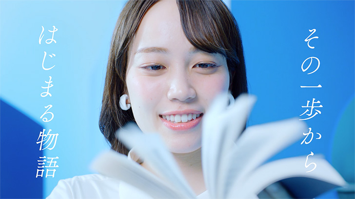 コンセプトムービーのキャプチャ:10枚中9枚目。本をめくる女性のアップ。テロップ「その一歩からはじまる物語」