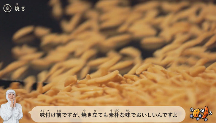 動画キャプチャ：機械から焼き上がった柿の種が出てくる様子と、味について解説する社員、それを聞いているたねっち&ぴーなっち