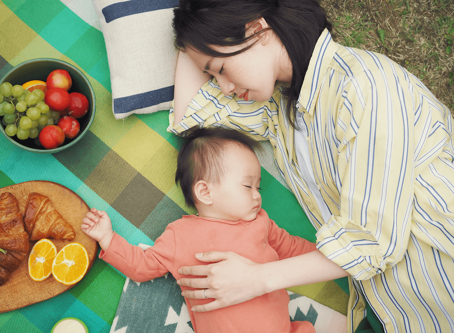写真:OLYMPUS OM-D E-M10 Mark IVプロモーションのメインビジュアル。レジャーシートの上でママと赤ちゃんが眠っている様子