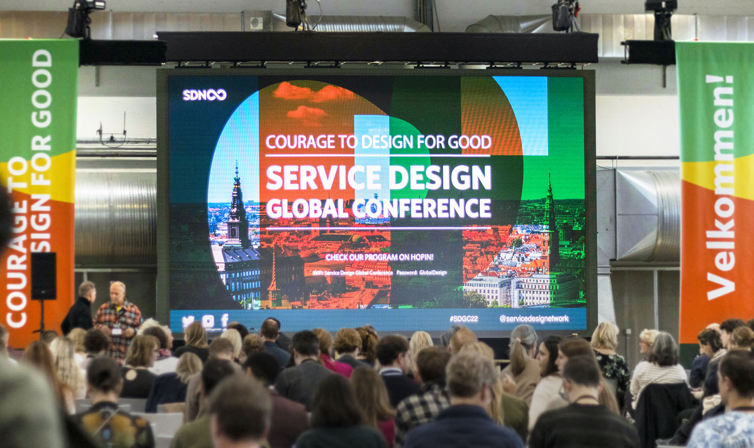 メイン画像：Service Design Global Conferenceの会場風景。参加者の前には大きなスクリーンがあり、イベントのメインビジュアルが映し出されることで、催しが開催される雰囲気を醸成している。