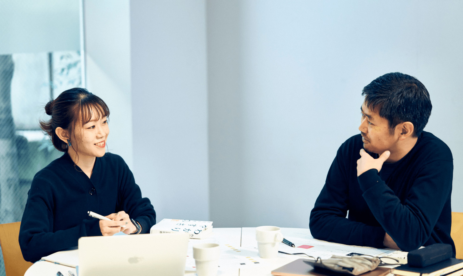 写真：長谷川、髙橋が机を面して対話している様子。