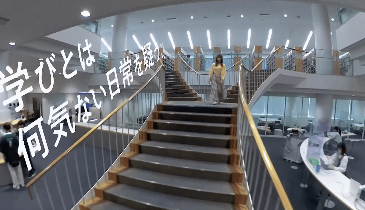 動画キャプチャ（4枚中3枚目）：図書館で階段を降りる学生と、「学びとは何気ない日常を疑うこと」のコピー