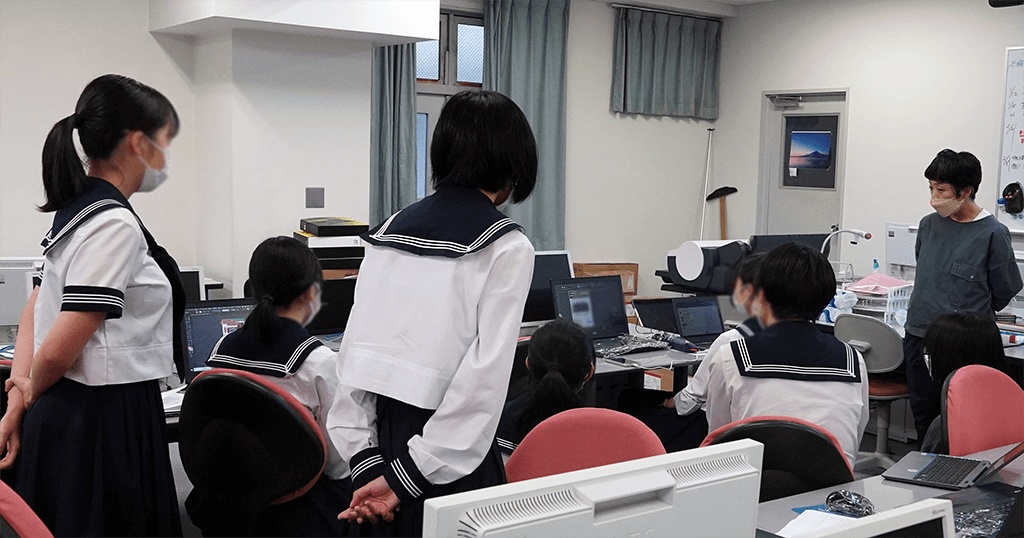 写真:PCに向かい作品を発表する生徒、それを聞くほかの生徒と講師