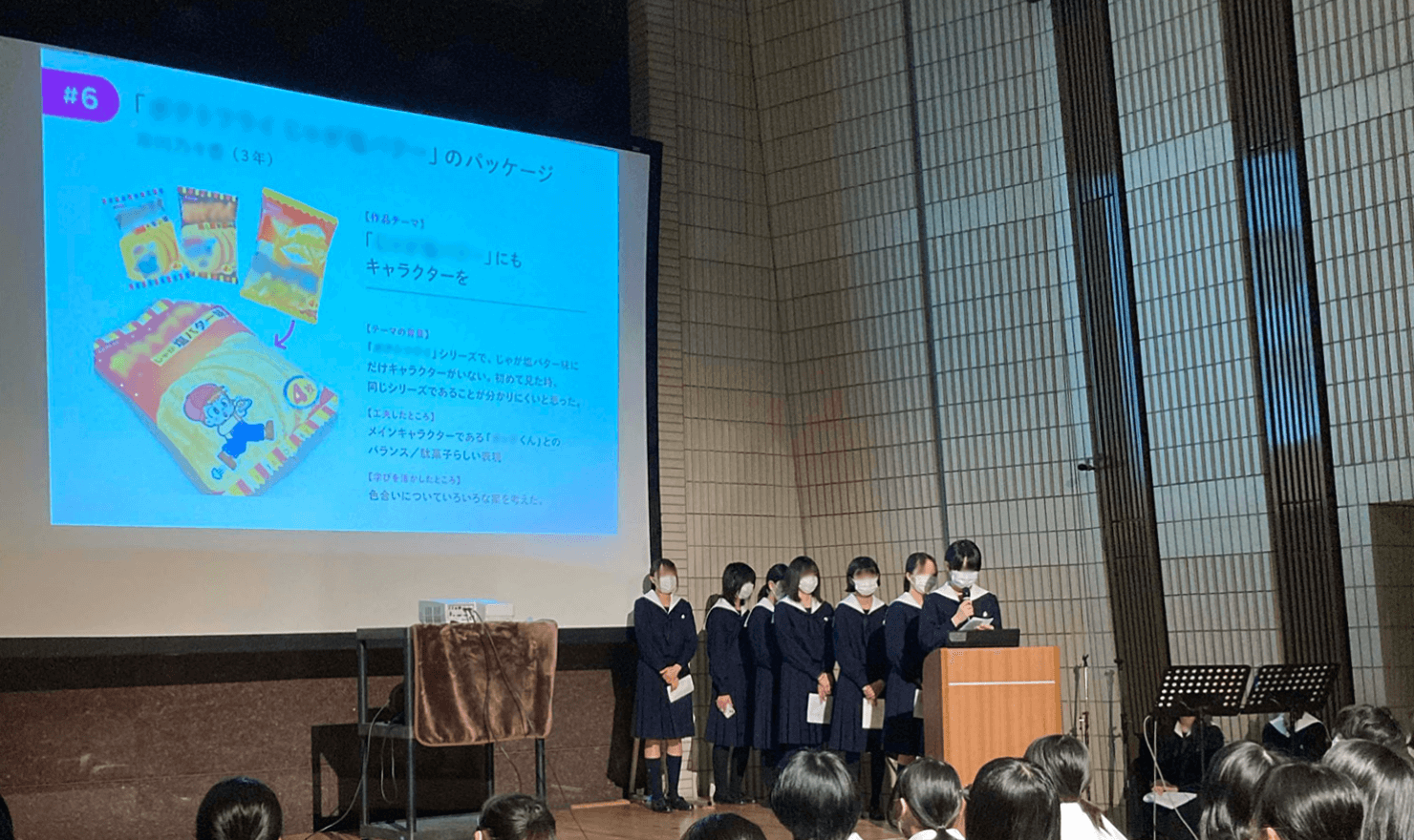 7名の生徒がステージにあがり、作品をスクリーン投影しながら発表している。