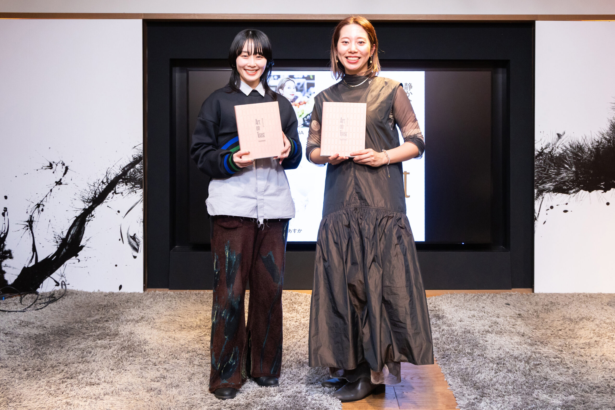 イベント会場で撮影された写真。作品集『Art on Toast 静かな生きもの」を手にした、著者SASAMANAとブックデザインを手がけた脇田あすか氏が並んで立っている。