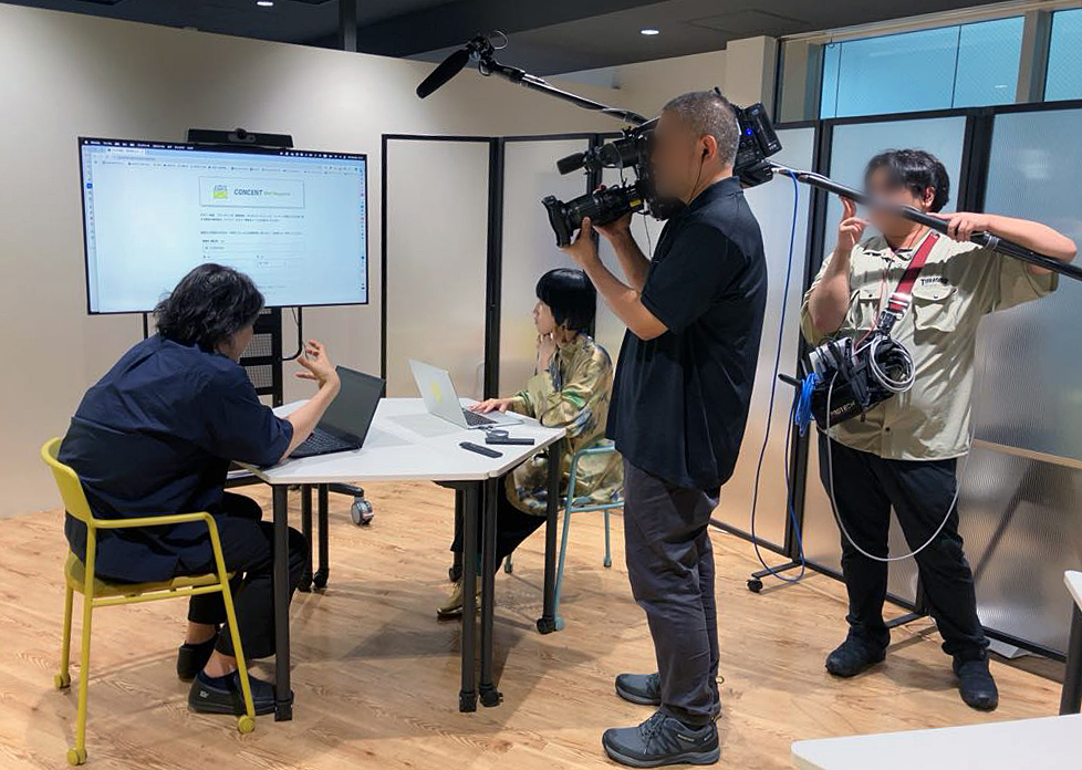 収録中の様子。加川と前田が向き合って座っている。その周囲に、収録用のマイク、ビデオカメラをもった二人の男性がいる