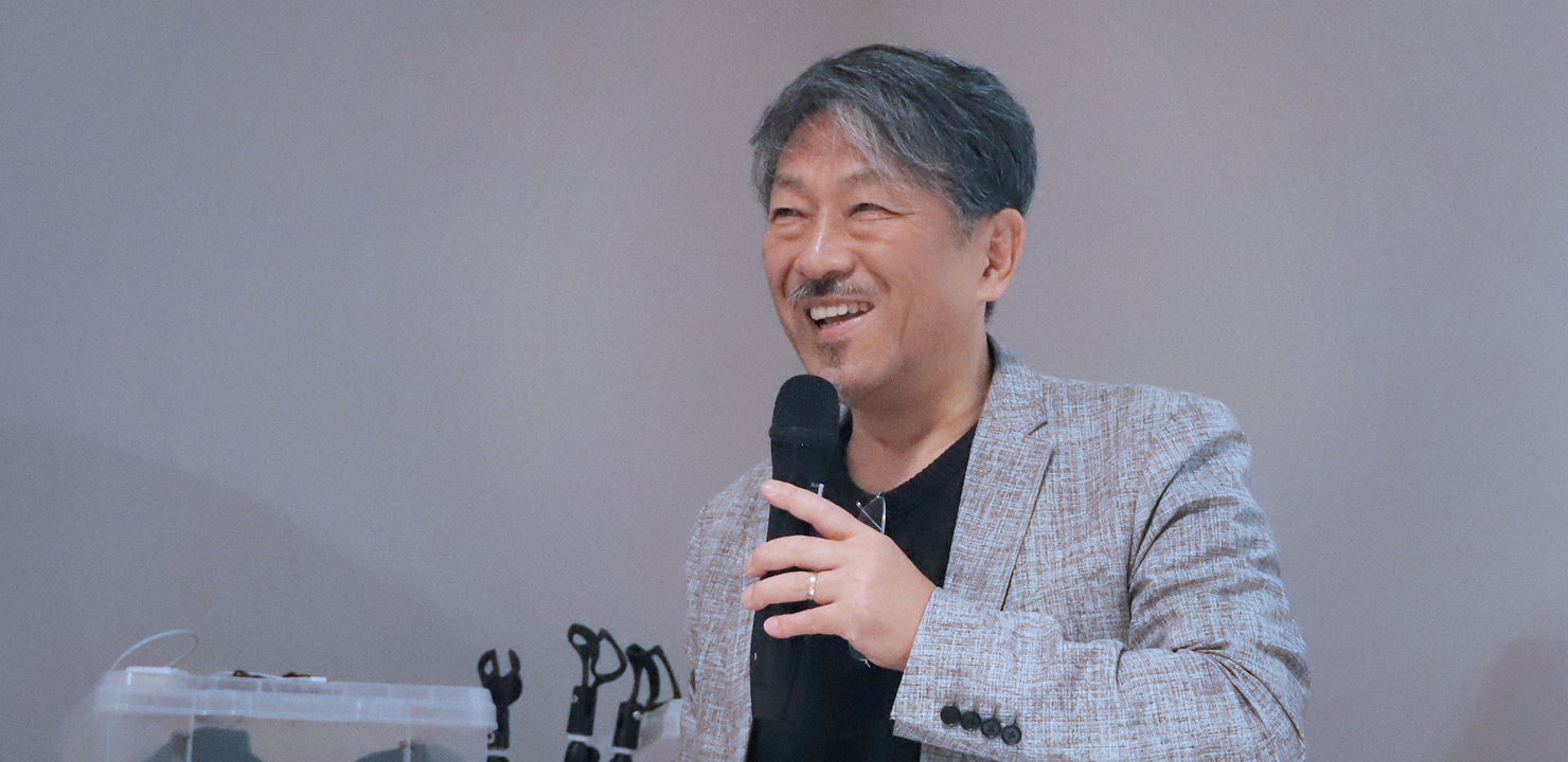 写真:村田智明氏がマイクを手に、笑顔で会場に向かって語っている様子。