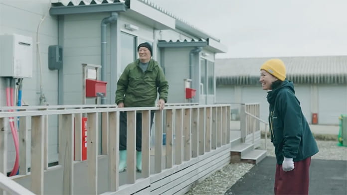 ドキュメンタリーの一場面。黄色い毛糸帽を被った女性と長靴を履いた男性が談笑している