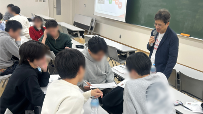 写真：中野が教室でマイクを持って講義している様子。