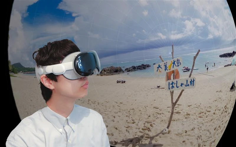Apple Vision Pro を装着した人とその人が視聴しているであろう映像カット。海を望む砂浜に「奄美大島ばしゃ山村」と書かれた看板がある。
