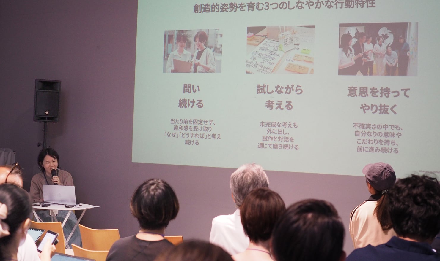 会場に登壇スライドが投影されている様子。創造的姿勢を育む行動特性として「問い続ける」「試しながら考える」「意思を持ってやり抜く」の3つが挙げられている。
